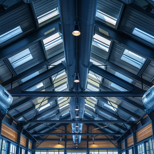 Industrial spiral ductwork and ridge ventilation installed in a modern steel barndominium ceiling to manage humidity and prevent condensation.