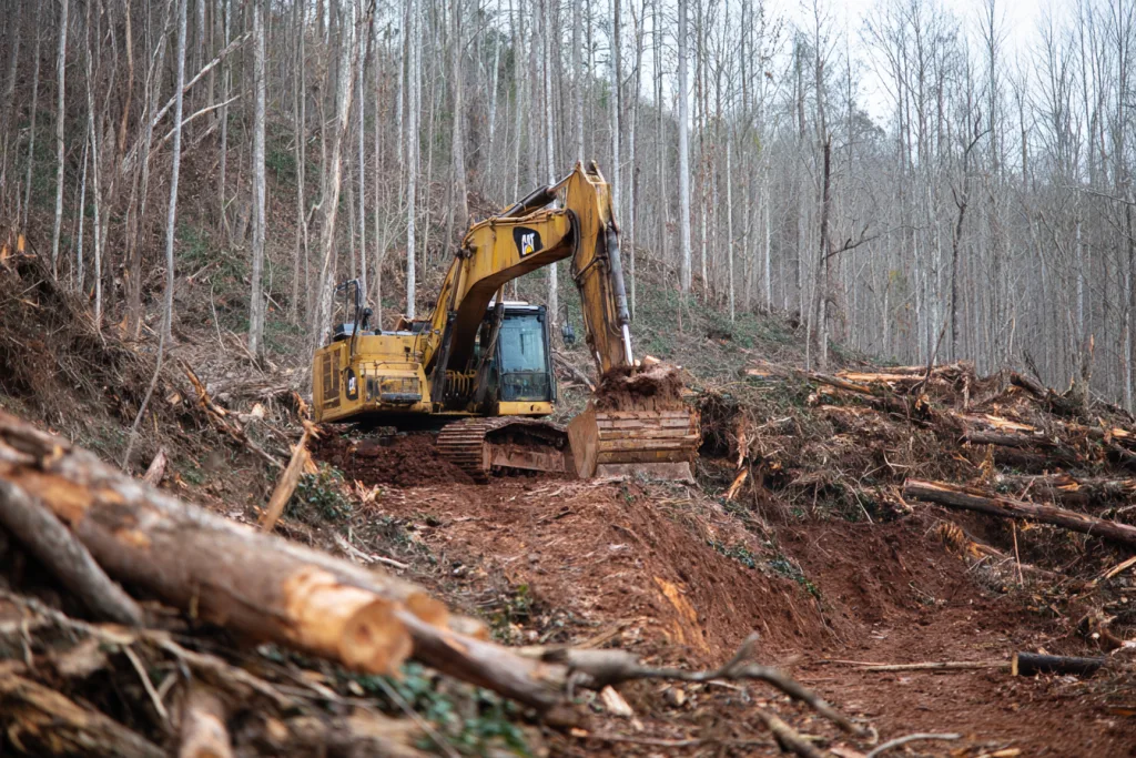 excavator grading land and removing stumps during barndominium site preparation process