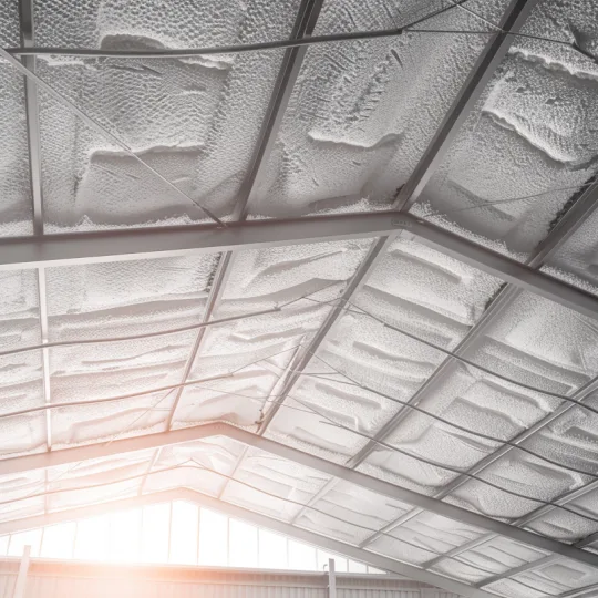 Thick white spray foam insulation applied between steel trusses and corrugated metal roofing in a modern barndominium.