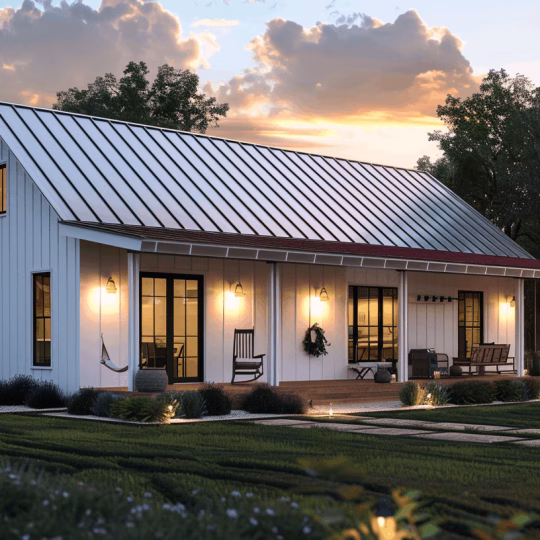 A compact white barndominium with a metal roof and an illuminated front porch at dusk, illustrating small floor plan efficiency.