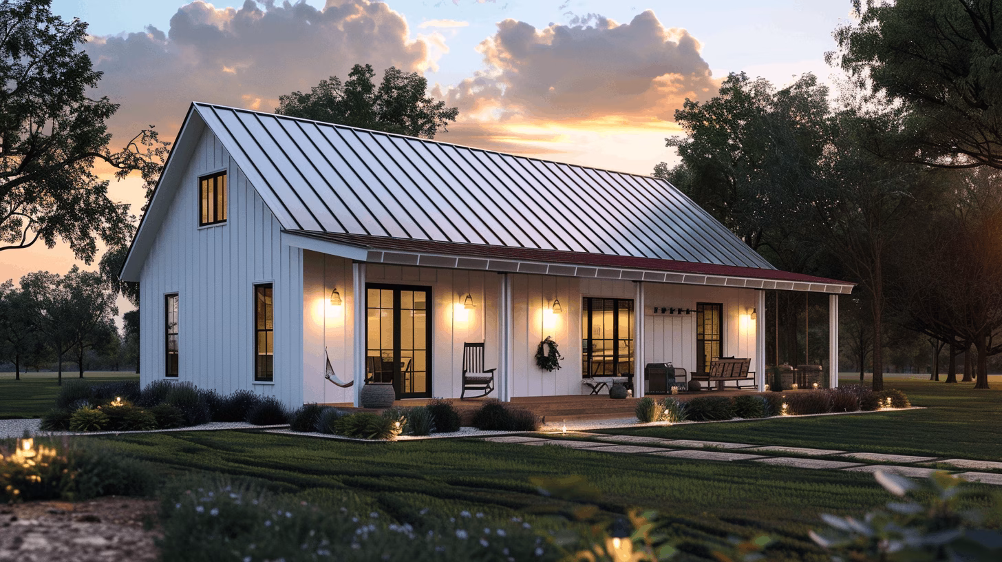 A compact white barndominium with a metal roof and an illuminated front porch at dusk, illustrating small floor plan efficiency.